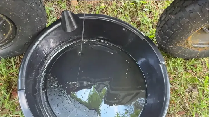 Drained break-in engine oil sitting in catch basin under sunlight