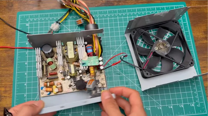 Opened ATX power supply enclosure showing internal circuit board, capacitors, and thick wiring harness