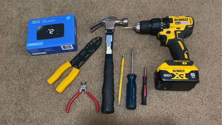 Hand tools including strippers, screwdrivers, and pencil laid out beside the existing thermostat