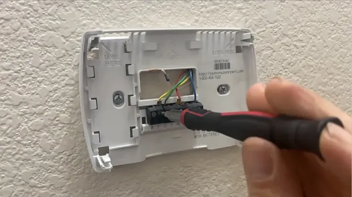 Flathead screwdriver loosening terminal screws on the old plastic thermostat baseplate