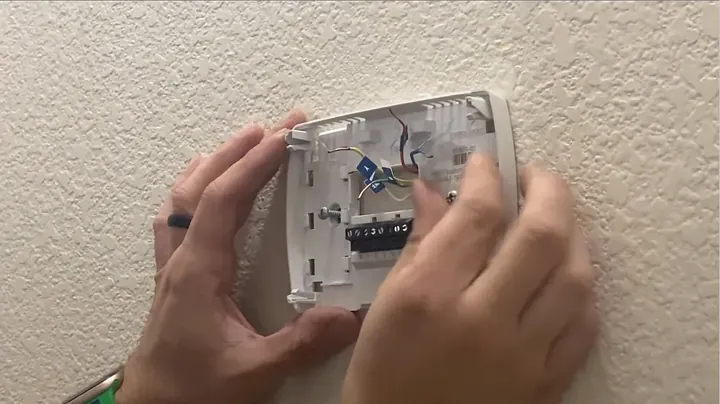Hands positioning the white plastic rectangular trim cover plate over the drywall opening