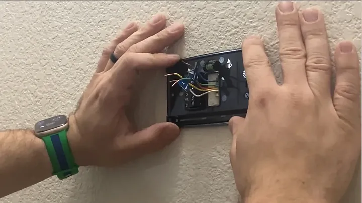 Hands feeding a bundle of labeled thermostat control wires through the backplate wire opening