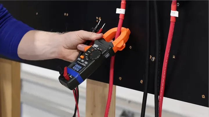 A DC clamp meter measuring current on a red positive wire, showing the organized wiring with pin terminals.