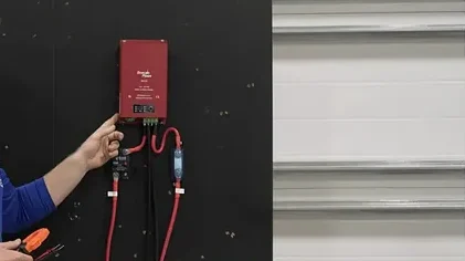 A hand pointing to the front panel button on the Sterling DC-DC charger, used for programming battery profiles.